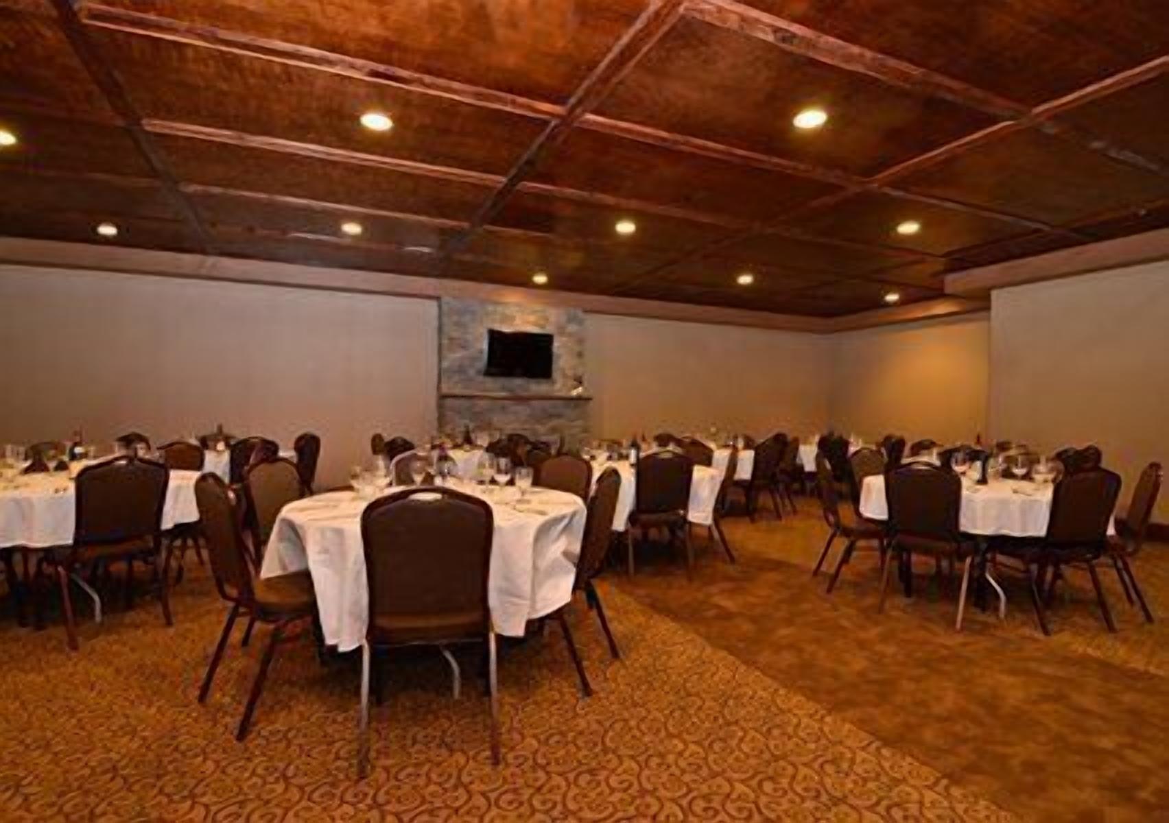 A banquet hall with round tables, chairs, and a patterned carpet.