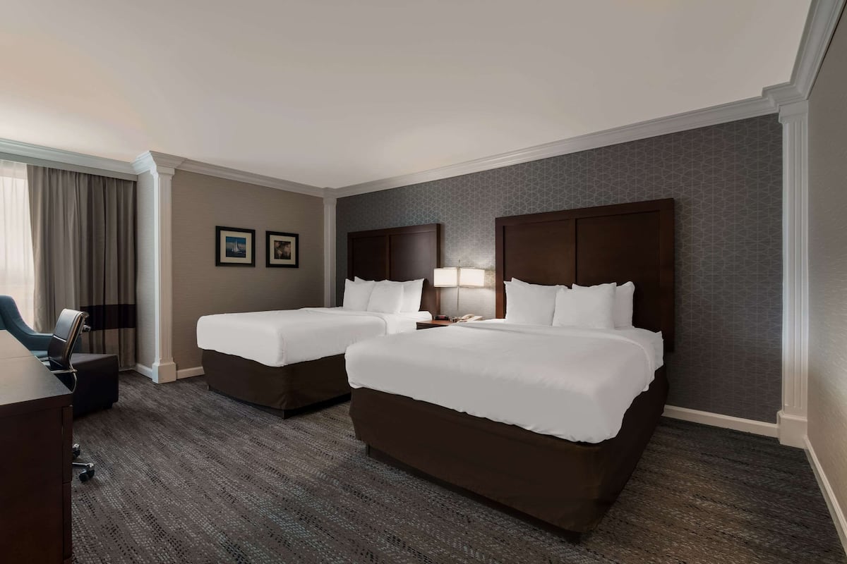 A hotel room with two beds, a desk, and a chair.