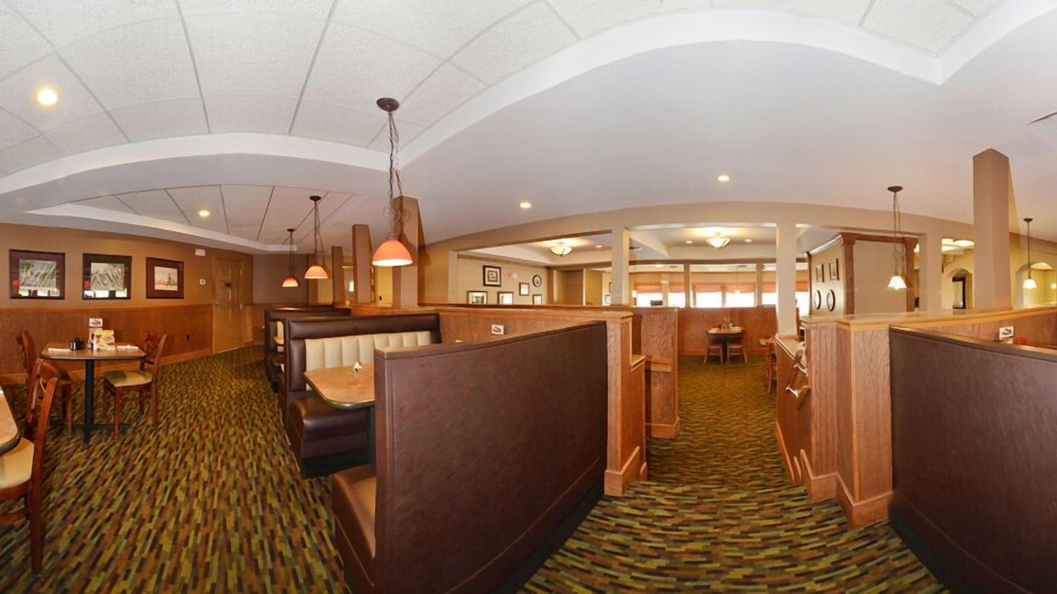 A hotel dining area with booth seating, a patterned carpet, and pendant lighting.