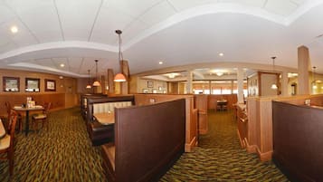 Ein Speisesaal eines Hotels mit Sitzboxen, einem gemusterten Teppich und Pendelleuchten.