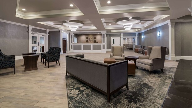 Un hall d’entrée spacieux au design moderne, comprenant un espace détente avec des canapés et des fauteuils, un comptoir d’accueil et un mur décoratif orné d’œuvres d’art encadrées.