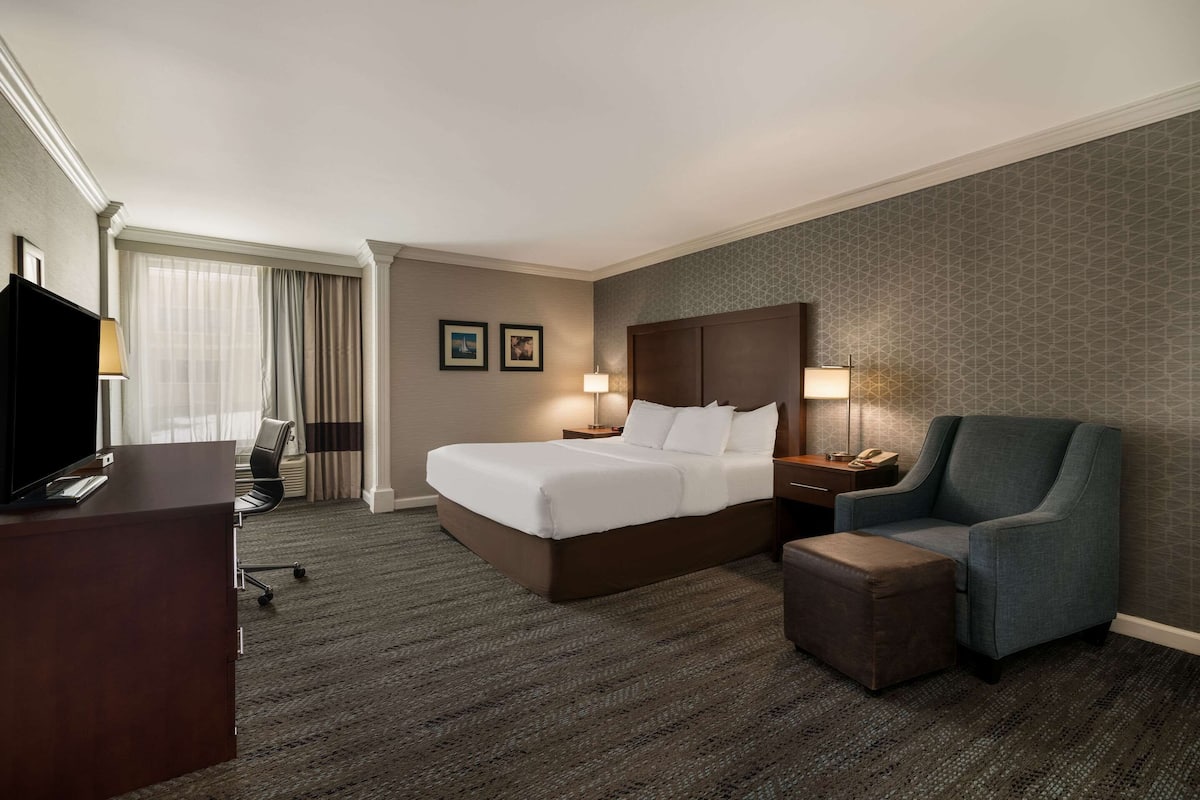 A hotel room with a bed, a desk, a chair, and a small ottoman.