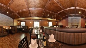 Un restaurant doté d’un plafond voûté très haut et d’une cheminée en pierre. Les tables sont dressées avec des serviettes blanches et des verres à vin.