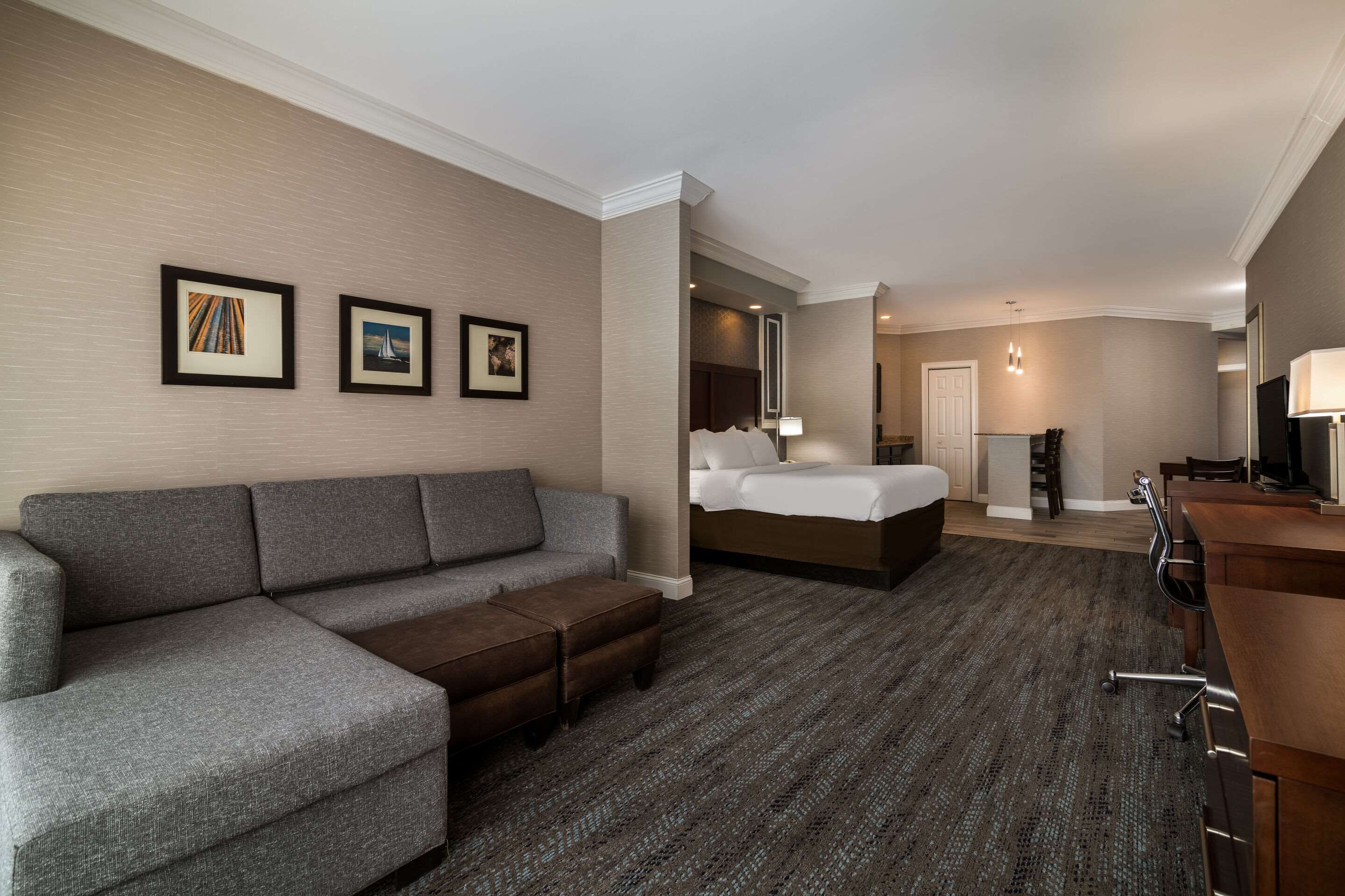 Une chambre d’hôtel avec un canapé gris, un lit avec du linge de maison blanc, un bureau en bois et un sol recouvert de moquette.