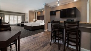 Une chambre d’hôtel comprenant un lit, un bureau, deux tabourets de bar, une kitchenette et un téléviseur.