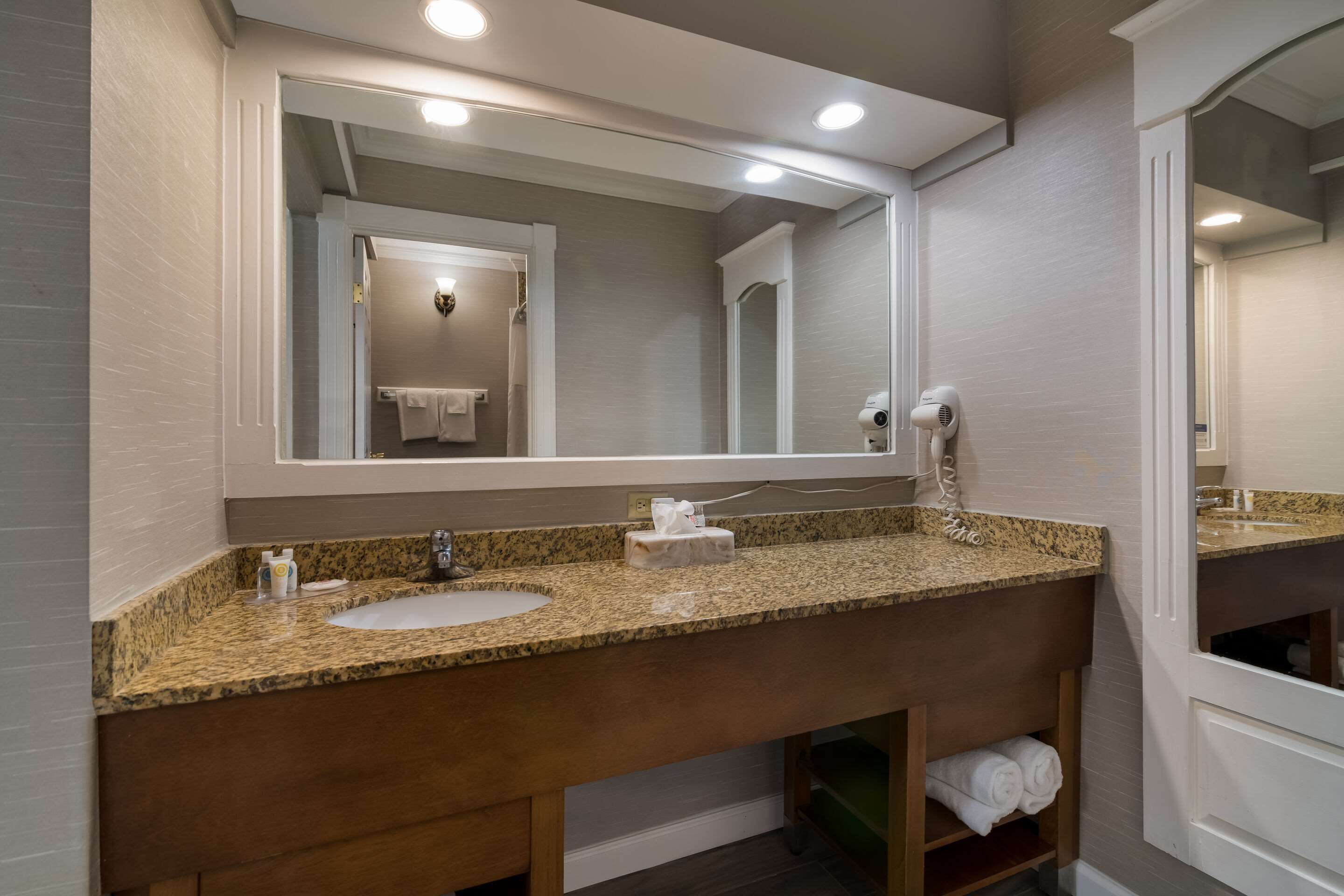 Une salle de bain dotée d’un lavabo avec un plan de toilette en granit, d’un grand miroir, d’un sèche-cheveux et d’un porte-serviettes.