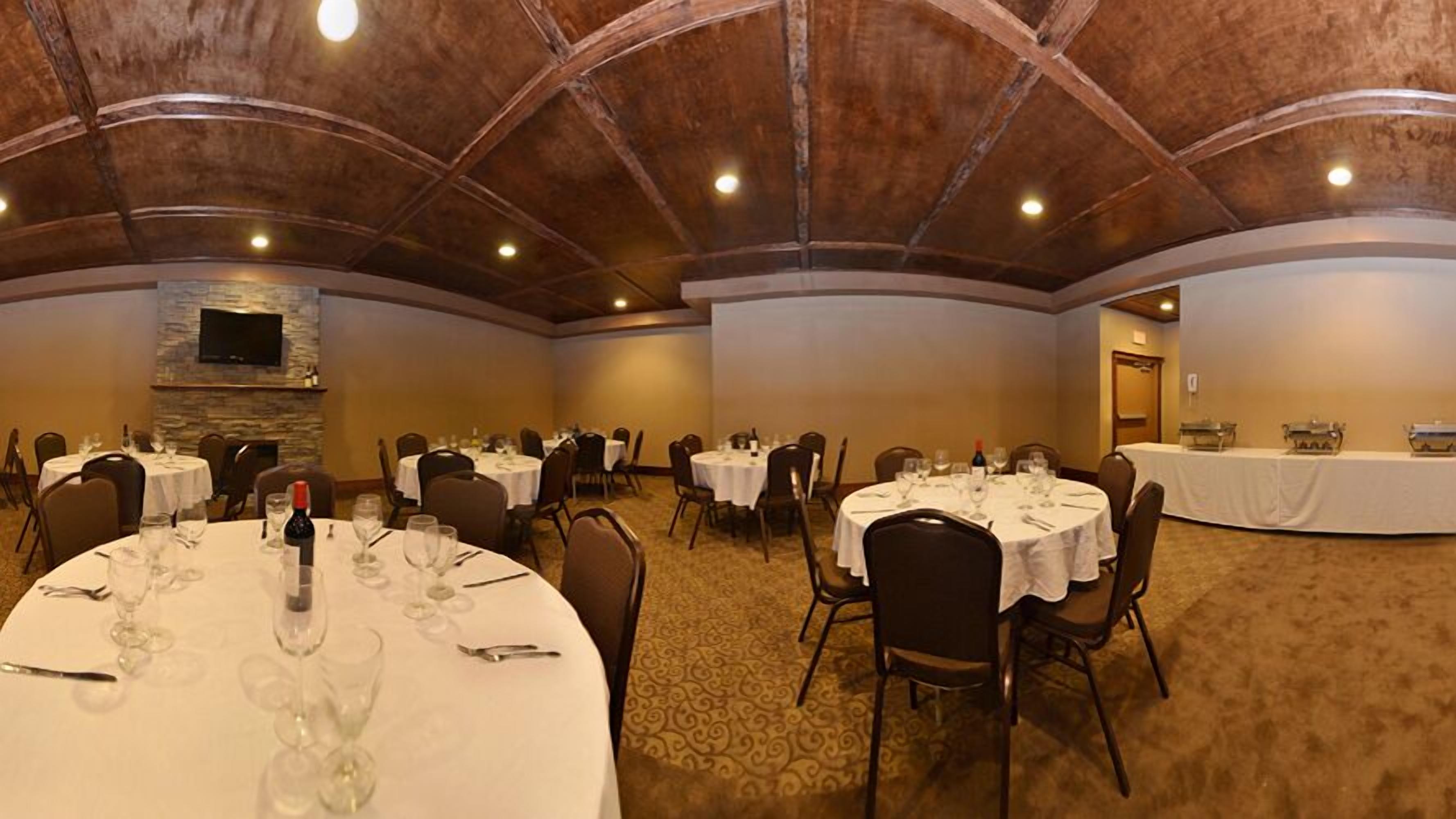 Un salón de banquetes con mesas redondas dispuestas para comer, equipado con copas de vino y cubiertos.