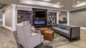 Un salon moderne comprenant un canapé d’angle, des fauteuils, des poufs, un téléviseur à écran plat et des étagères intégrées ornées d’objets décoratifs.