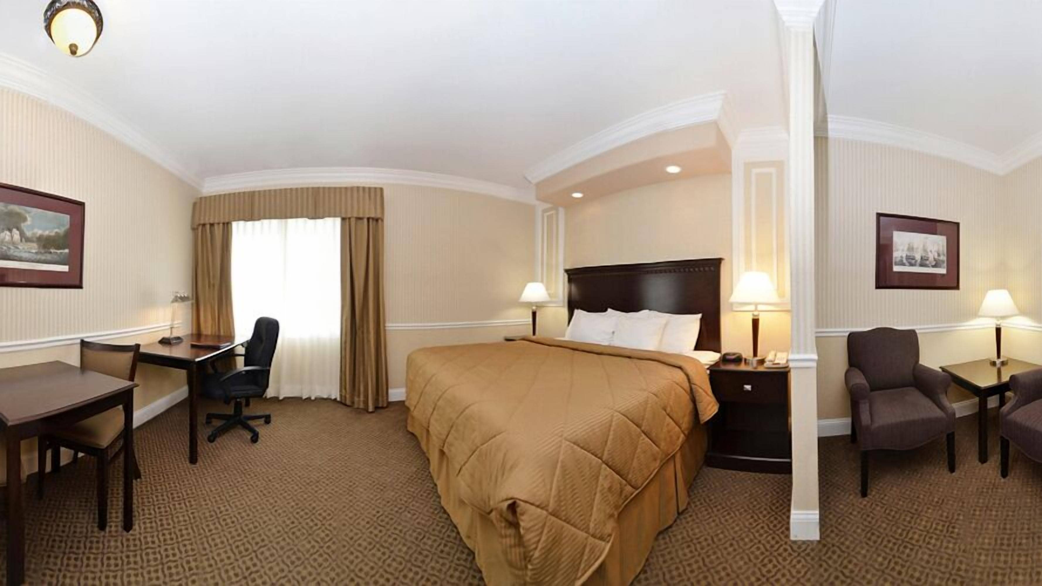 Habitación de hotel con una cama grande, un escritorio, una silla y una mesita de noche con lámpara.