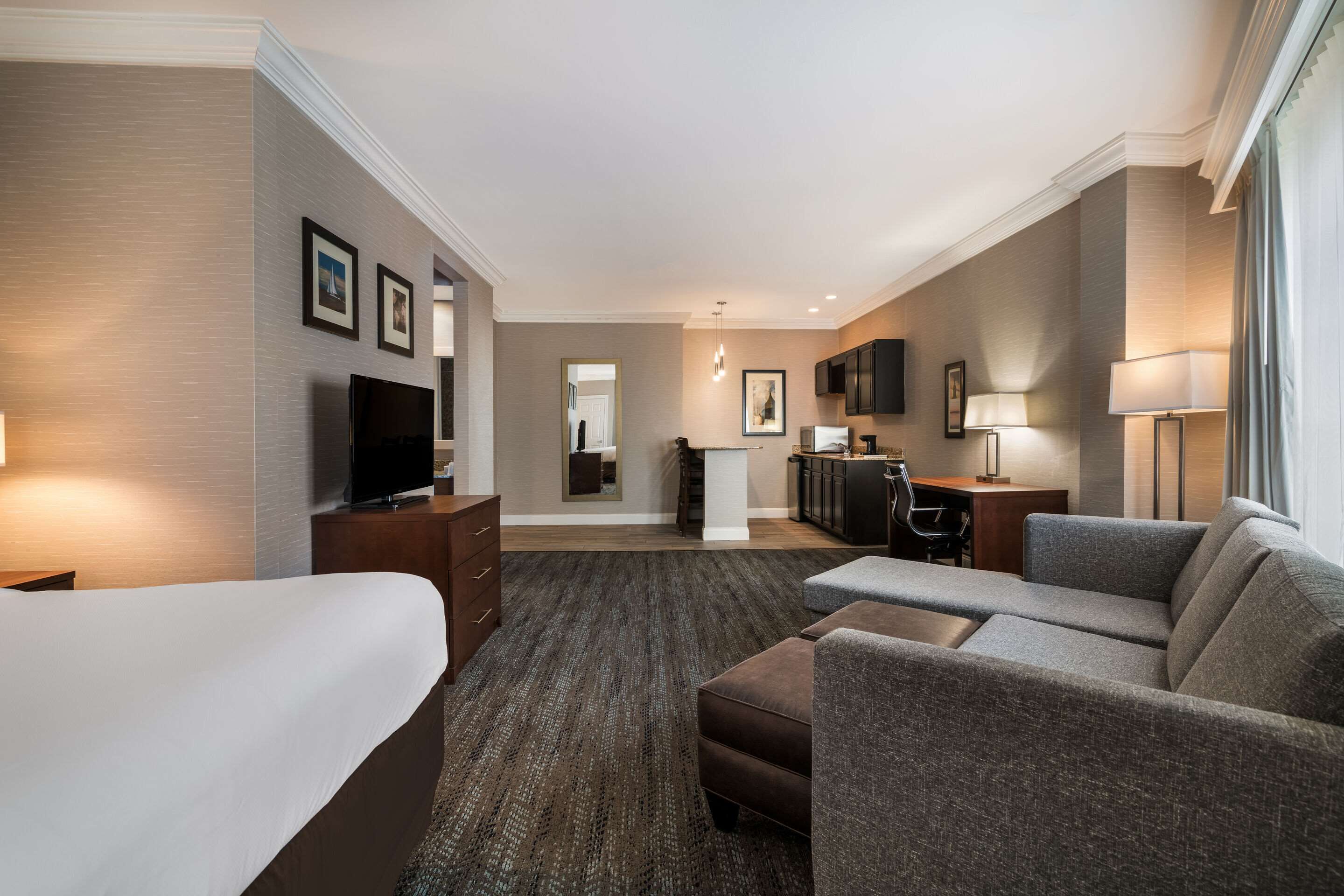 A hotel room with a bed, a sofa, a desk, a TV, and a mirror.