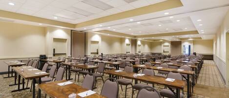 A large conference room with rows of tables and chairs, equipped with nameplates and pens.