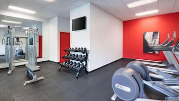 A gym with exercise equipment, a TV, and a red accent wall.