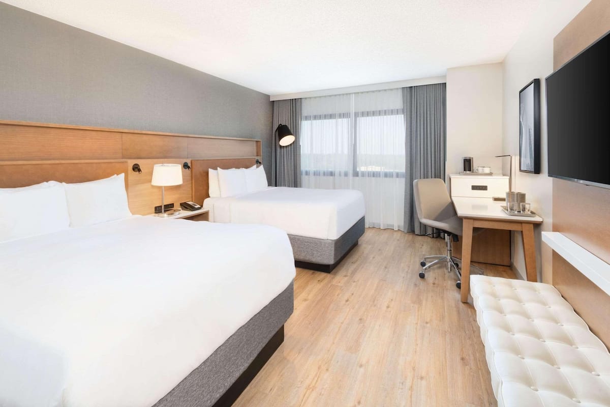Una habitación de hotel con dos camas, un escritorio, una silla, un televisor y una ventana con cortinas.