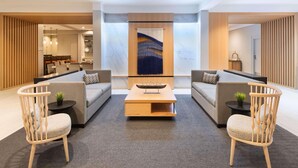 Un lobby moderno con un conjunto de sofás, sillas de madera, una mesa de centro y un elemento decorativo en la pared.