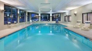 Una piscina interior con agua azul cristalina, rodeada de ventanas que ofrecen vistas de la ciudad de noche.