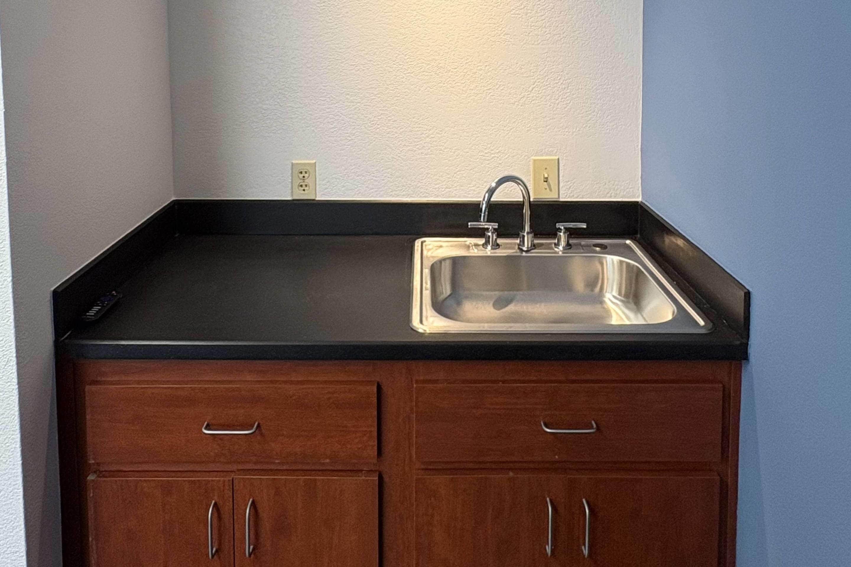 Cocina con encimera negra, pileta de acero inoxidable y armarios de madera.