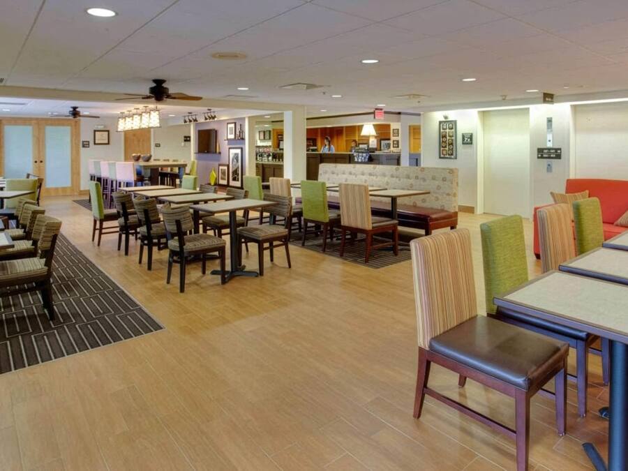 A hotel lobby with multiple dining tables, chairs, a reception desk, and a bar area.