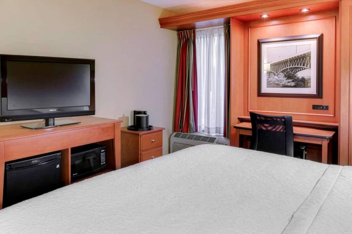 A hotel room with a bed, a TV, a desk with a chair, a microwave, a coffee maker, and a picture on the wall.