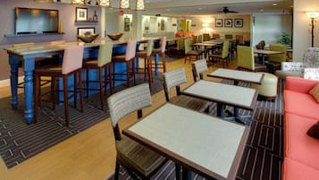 Um saguão de hotel com área de bar, mesas de jantar e um espaço de estar com sofás.