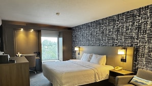 A hotel room with a large bed, bedside tables, a desk, a chair, and a view of the outdoors.