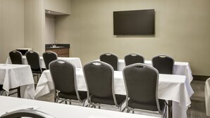 A conference room with tables and chairs, a flat-screen TV, and a small kitchenette area.