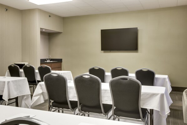 A conference room with tables and chairs, a flat-screen TV, and a small kitchenette area. - Pittsburgh Airport Inn and Suites (Coraopolis)