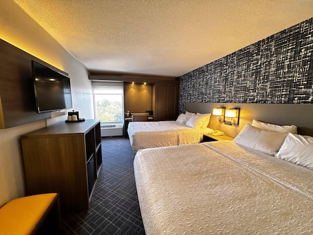 A hotel room with two beds, a desk, a TV, and a window with a view.