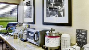 A kitchen area with a coffee machine, a microwave, and a kettle. There are framed pictures on the wall and a sign that says "Healthy Zone".