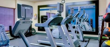 Une salle de sport équipée de tapis de course, de vélos d’appartement et d’un mur recouvert de miroirs.