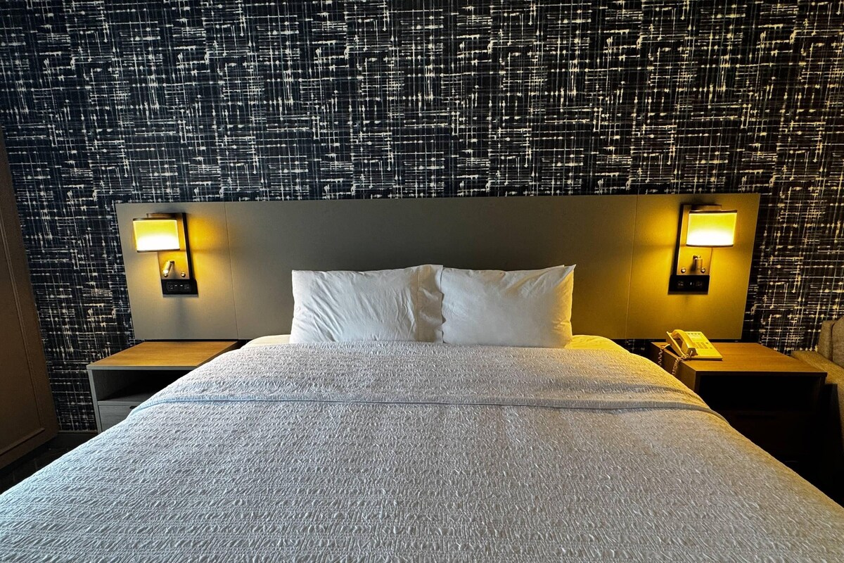 A hotel room with a large bed, two bedside tables, and a patterned wall.