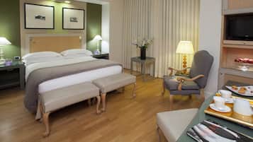 A hotel room with a bed, bedside tables, a chair, a desk with a tray of breakfast items, and a television.