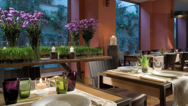 Un comedor con mesas dispuestas para el servicio, destacando centros de mesa florales, velas y cristalería.