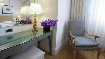 A modern hotel room with a glass desk, a wooden chair, and a vase of purple flowers.
