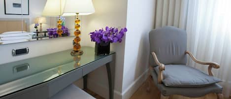 A modern hotel room with a glass desk, a wooden chair, and a vase of purple flowers.