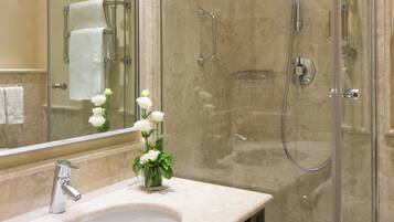 Un baño moderno con ducha envuelta en cristal, un lavamanos con espejo y un florero con flores blancas sobre la encimera.