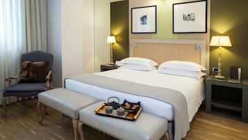 A hotel room with a large bed, two bedside tables with lamps, a chair, a bench with a tray of breakfast items, and two framed pictures on the wall.