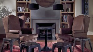 Un salón con dos sillones de cuero, una mesa de centro y una chimenea. Hay estanterías a cada lado de la chimenea y dos lámparas de pie.