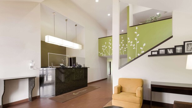 A modern lobby with a reception desk, a staircase with a green accent wall, and a seating area with a sofa and armchair. - Sleep Inn Tanglewood (Roanoke)