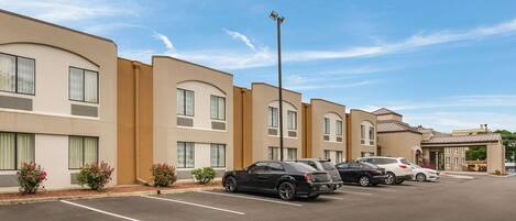 A row of hotel buildings with parking spaces and a clear sky.