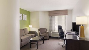 A hotel room with a sofa, armchair, desk, and television. - Sleep Inn Tanglewood (Roanoke)