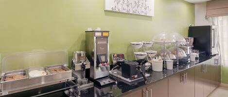 A breakfast bar with a waffle maker, coffee machine, and a variety of food containers.