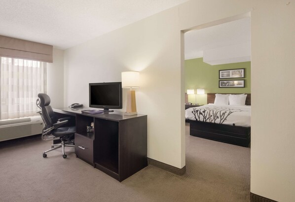 A hotel room with a desk, chair, television, lamp, and a bed with a canopy.