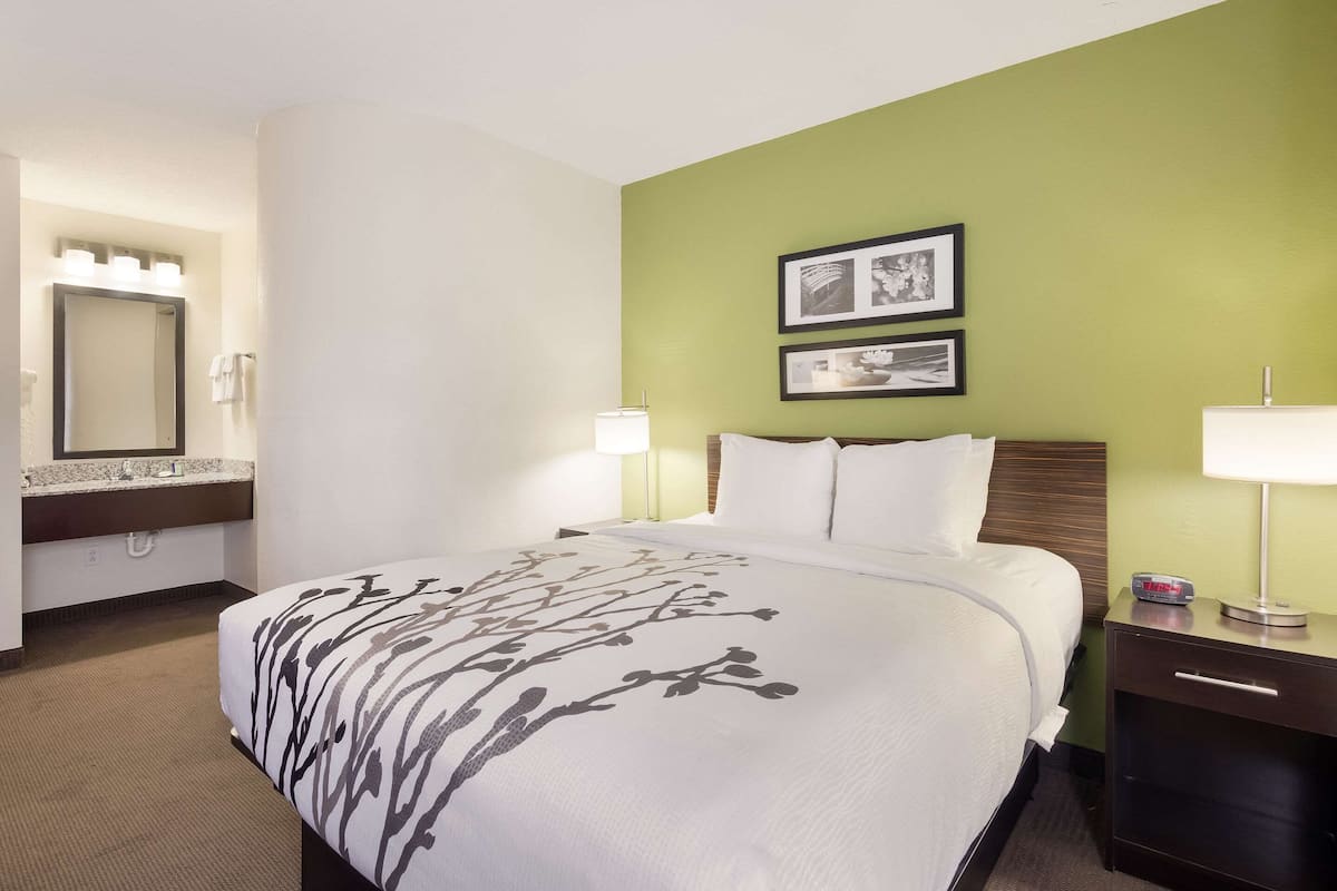 A hotel room with a bed, a nightstand, a lamp, a mirror, and two framed pictures on the wall.