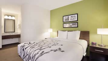 A hotel room with a bed, a nightstand, a lamp, a mirror, and two framed pictures on the wall.