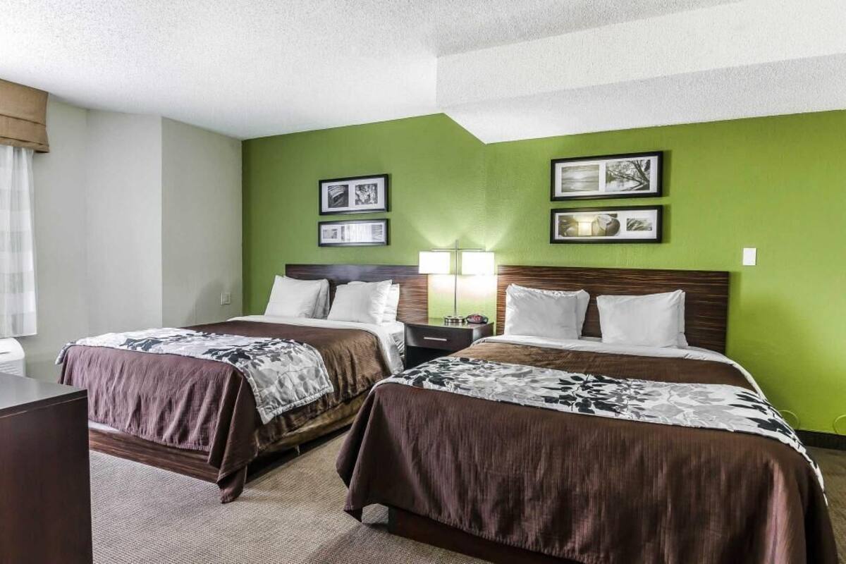 A hotel room with two beds, a nightstand, a lamp, and framed pictures on the wall.