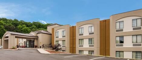 A multi-story hotel with a modern design, featuring a central entrance with a covered area and a parking lot in front.