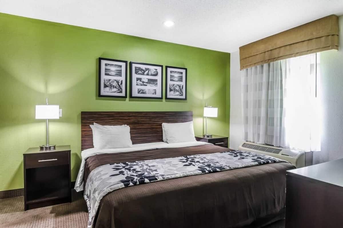 A hotel room with a bed, two bedside lamps, a window with curtains, and three framed pictures on the wall.