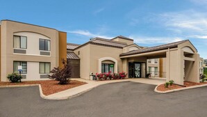 A modern building with a curved driveway, multiple entry points, and a landscaped entrance area with red flowers. - Sleep Inn Tanglewood (Roanoke)