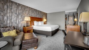 A hotel room with a bed, a sofa, a coffee table, a desk, and a lamp. - The Academy Hotel Colorado Springs (Colorado Springs)