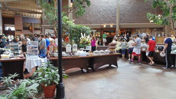 Un concurrido patio de comidas cubierto con varias mesas y gente.